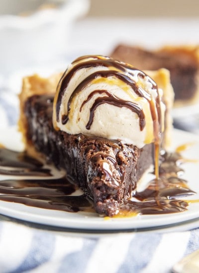 A slice of brownie pie topped with vanilla ice cream and chocolate syrup on top.
