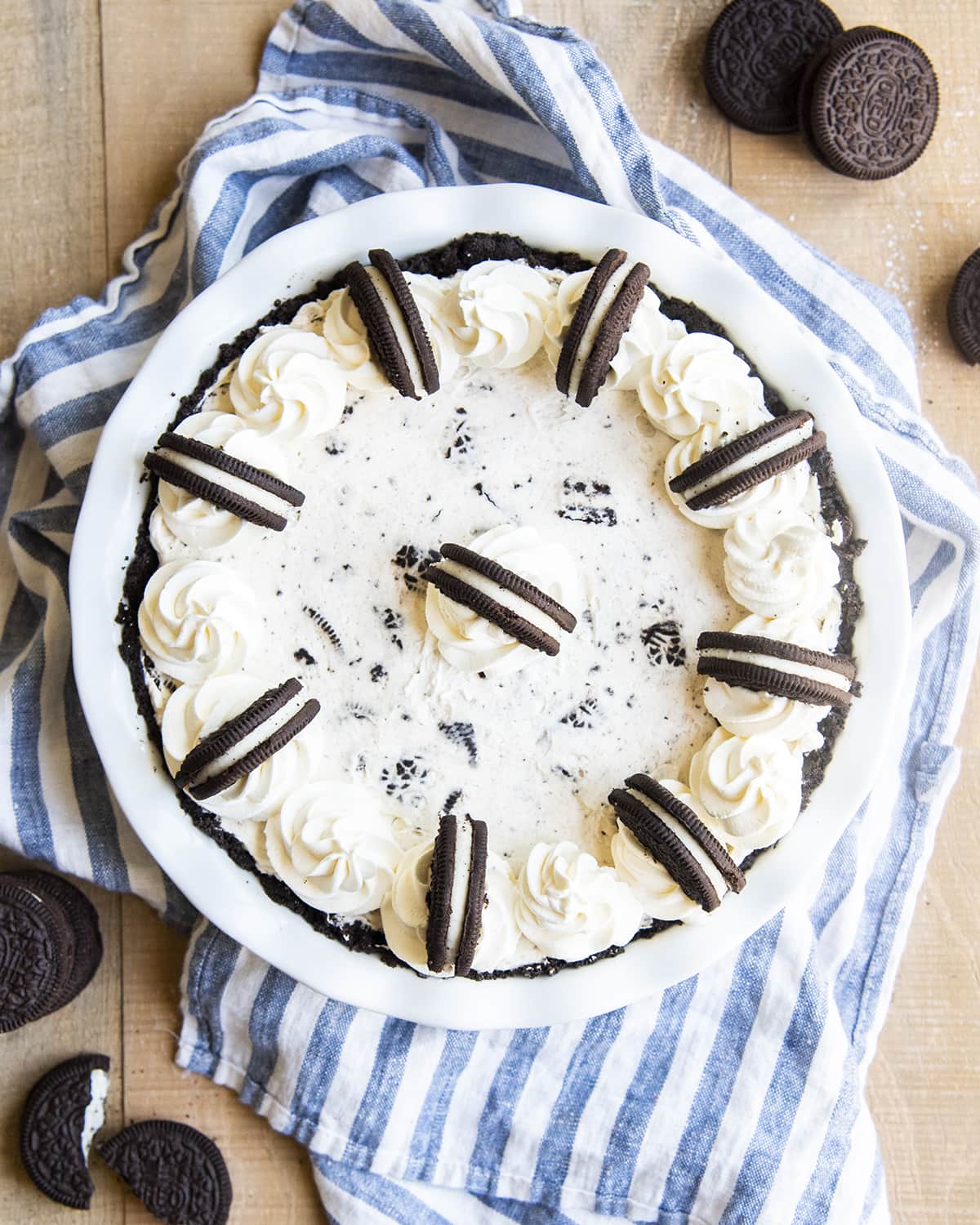 An overhead shot of a cream pie with pieces of Oreo in it, and topped with swirls of whipped cream and half Oreo pieces on the edges.