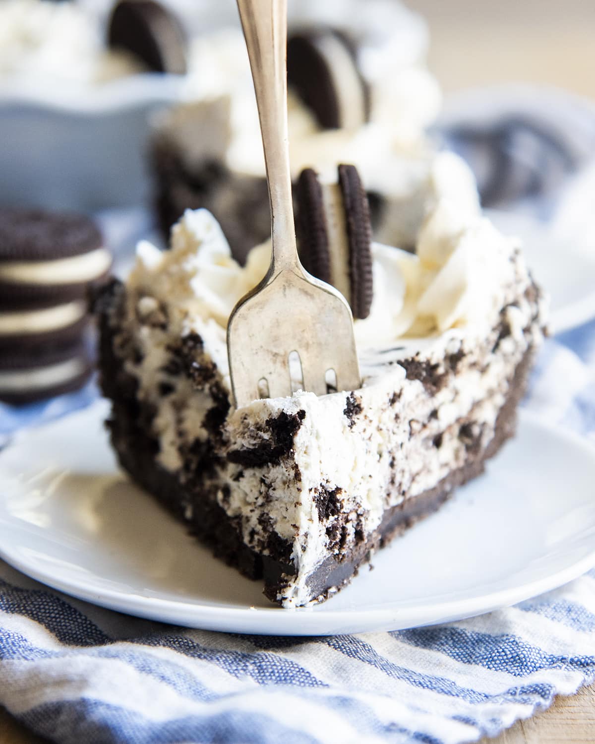 A piece of cookies and cream pie on a plate with a fork in the front taking a bite out.