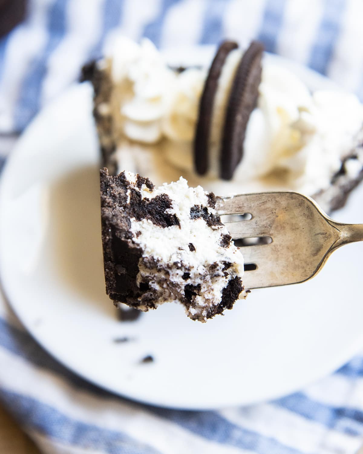 A bite of Oreo pie on a fork being held above a plate.