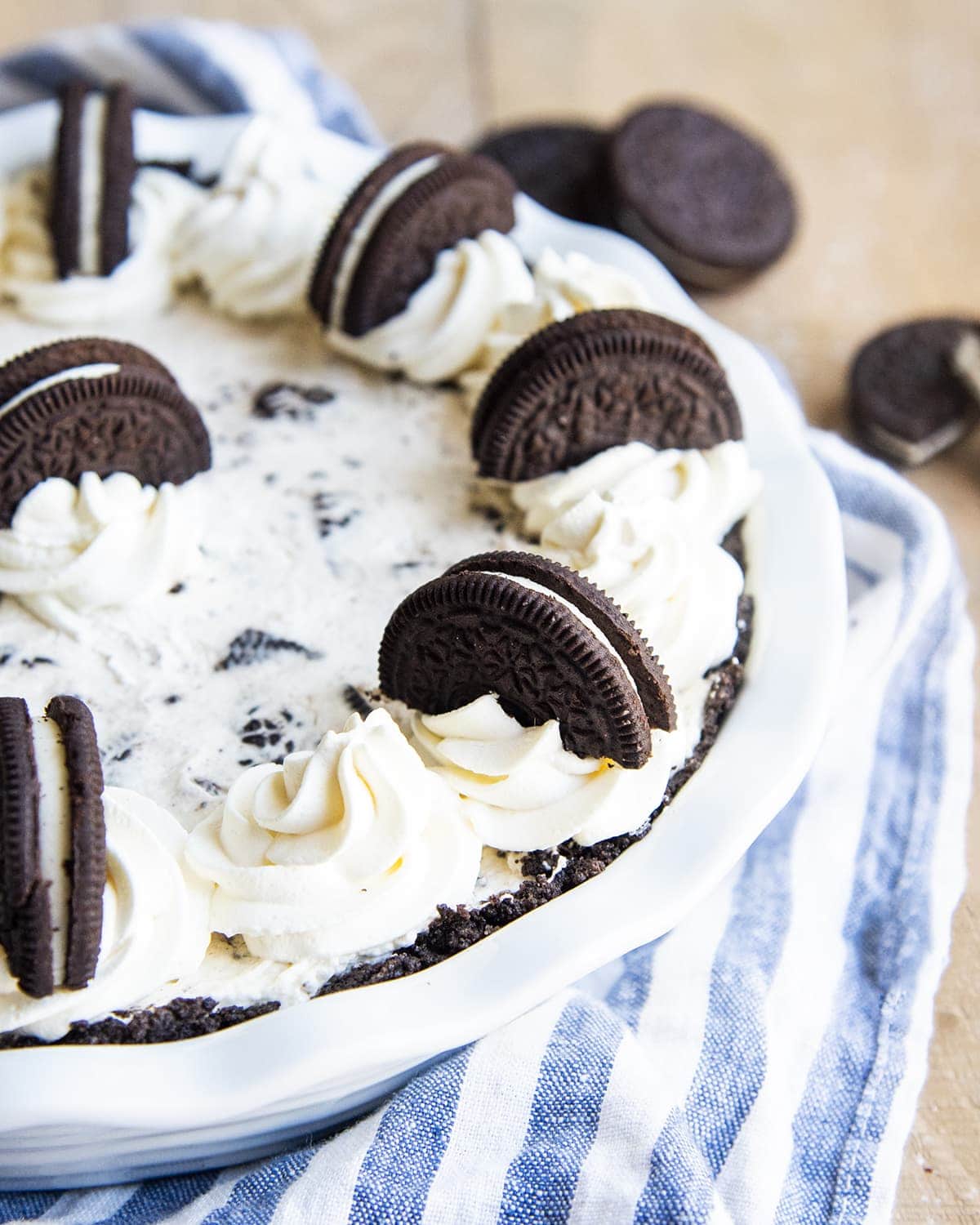 A cookies and cream pie in a white pie dish, topped with whipped cream and Oreos.