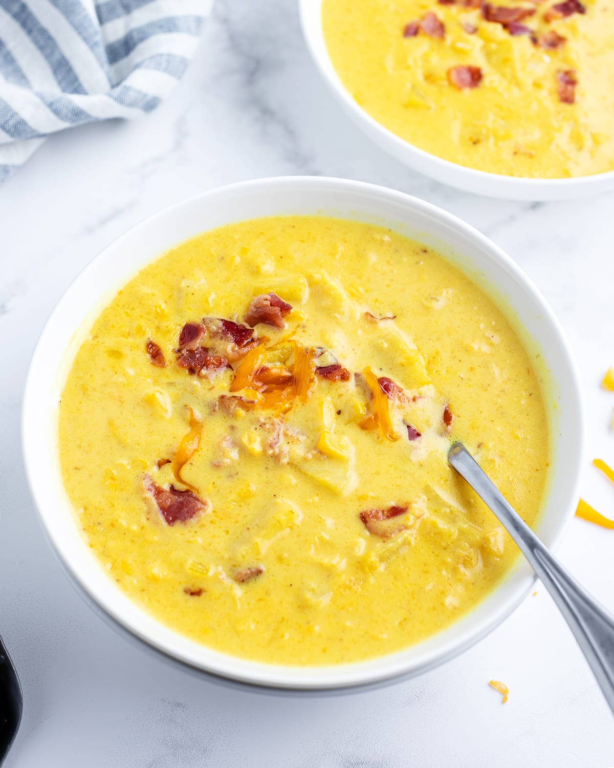 A white bowl full of corn chowder, topped with shredded cheese and bacon bits.