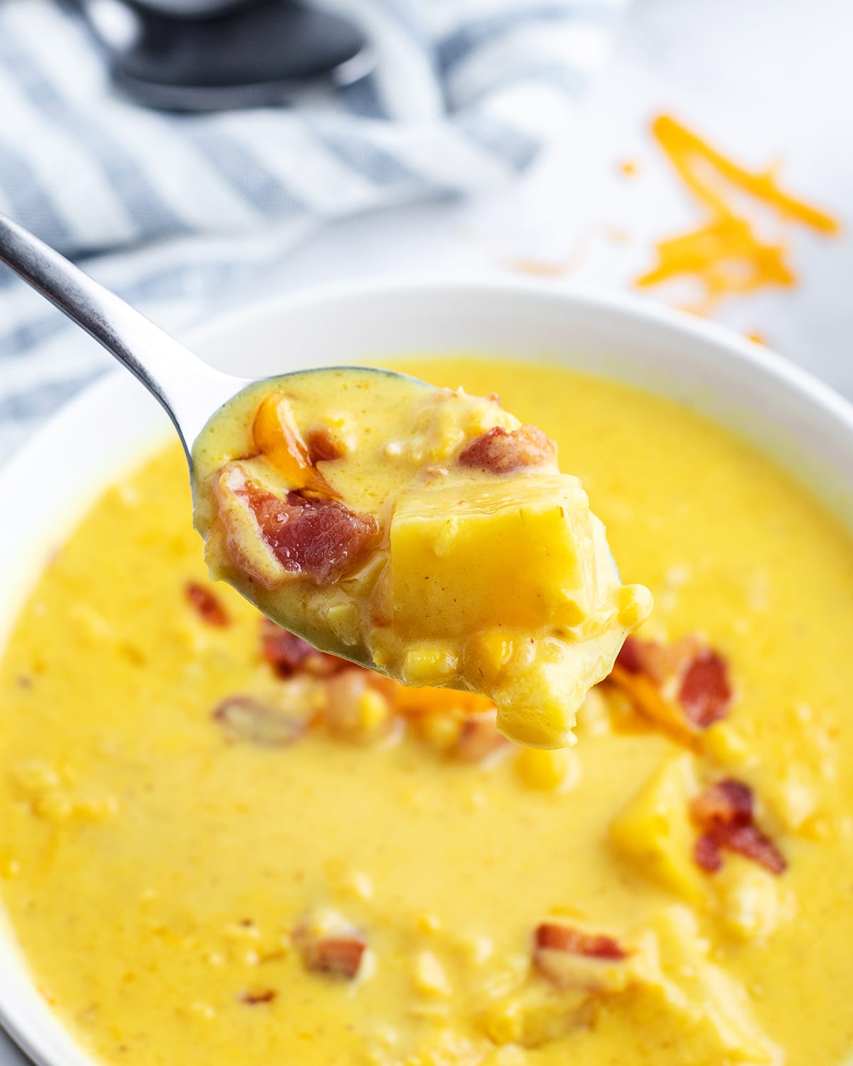 A spoonful of cheesy corn chowder above a bowl of the soup.