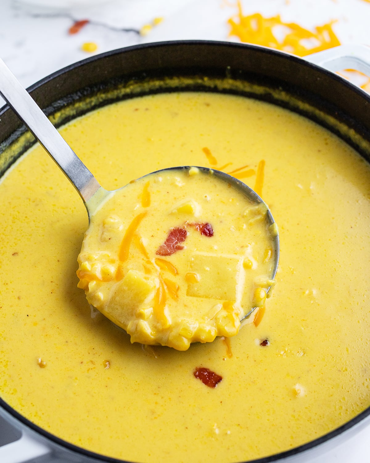 A pot of corn chowder that is very yellow with a big ladle of soup being helf above it.