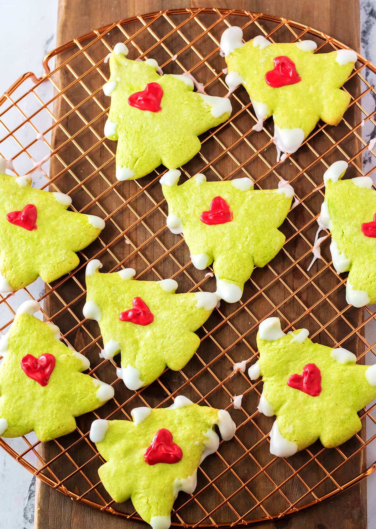 Grinch Christmas Tree Cookies on a cooling rack, they are green tree shaped cookies with a red heart decorated on them.