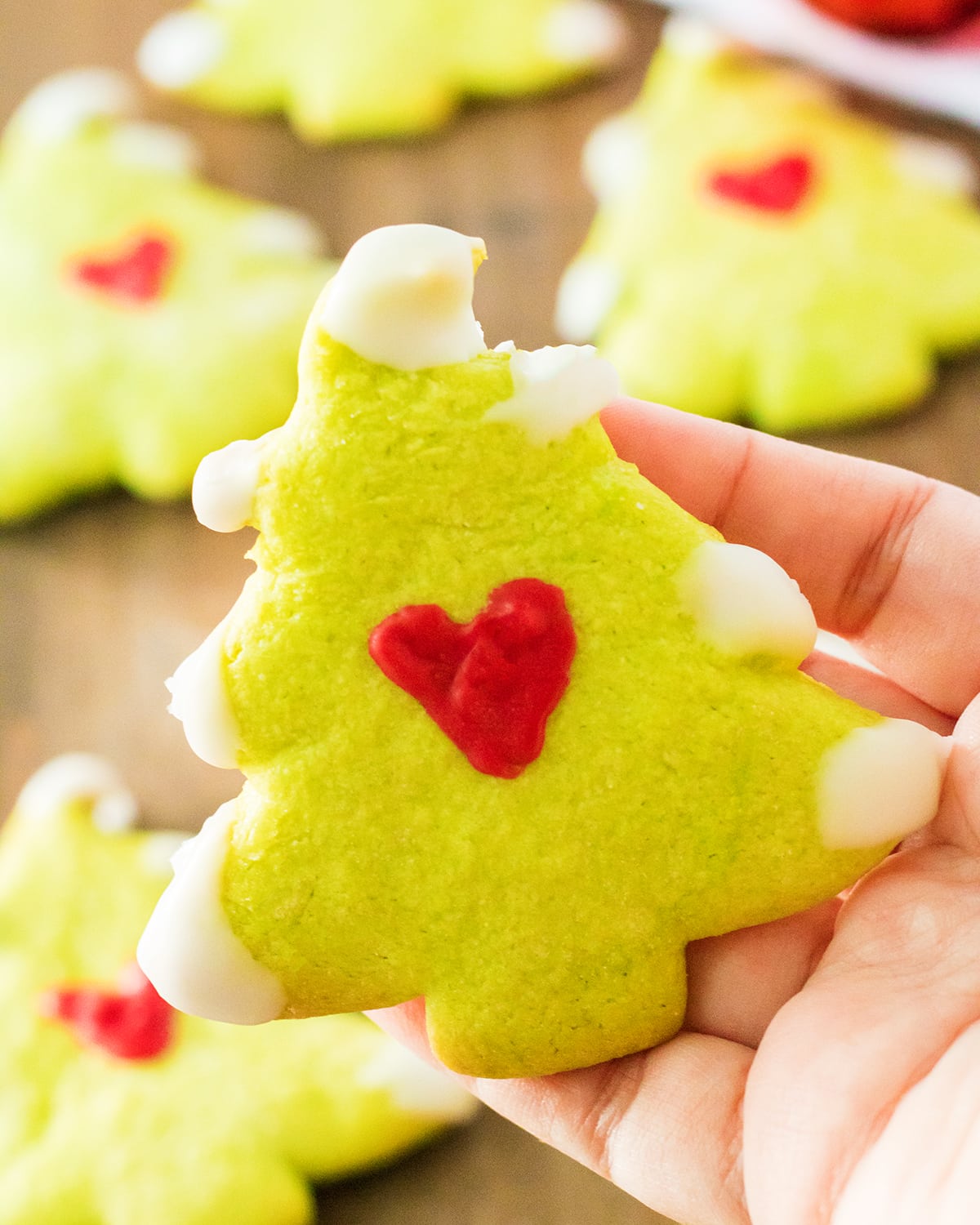 A hand holding a Grinchy Christmas tree sugar cookie.