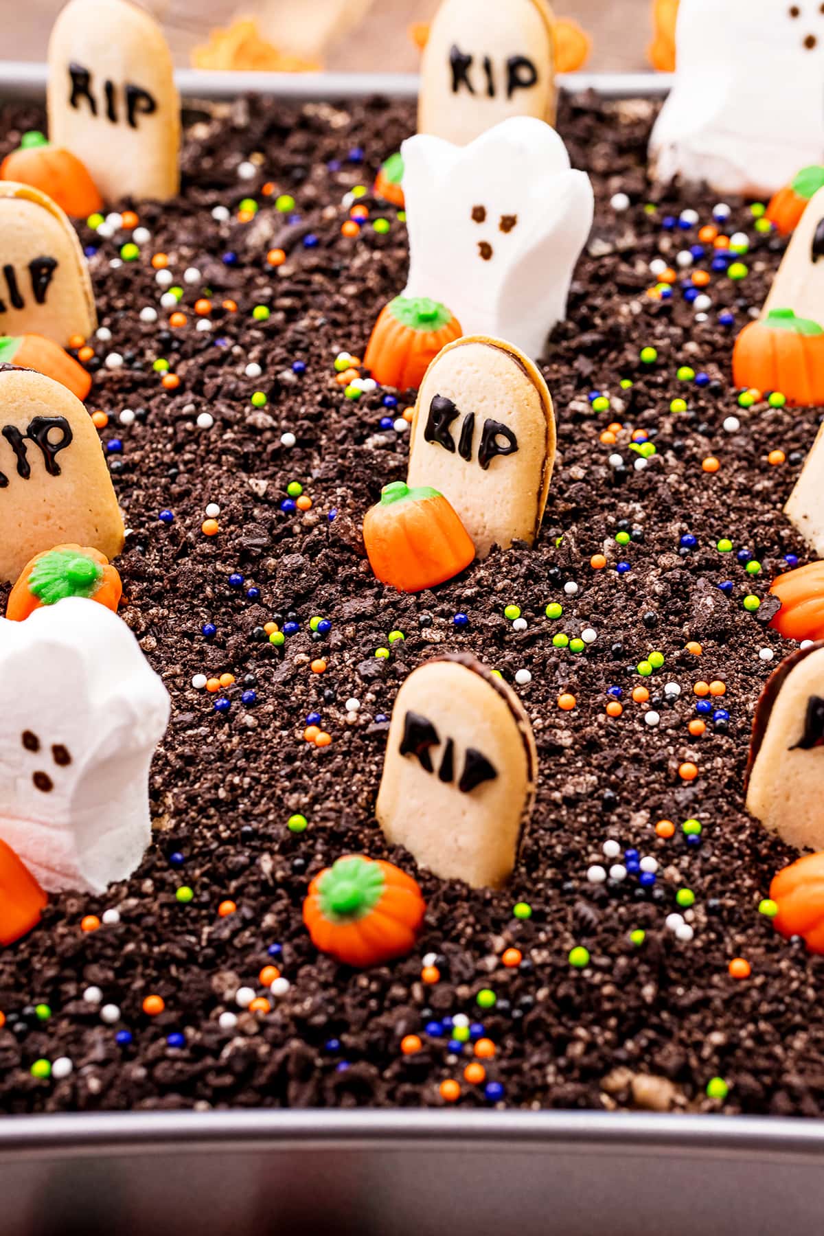 The top of a Halloween dirt cake that is covered in Oreo cookie crumbs, and Milano cookies decorated to say RIP, and ghost Peep Marshmallows.