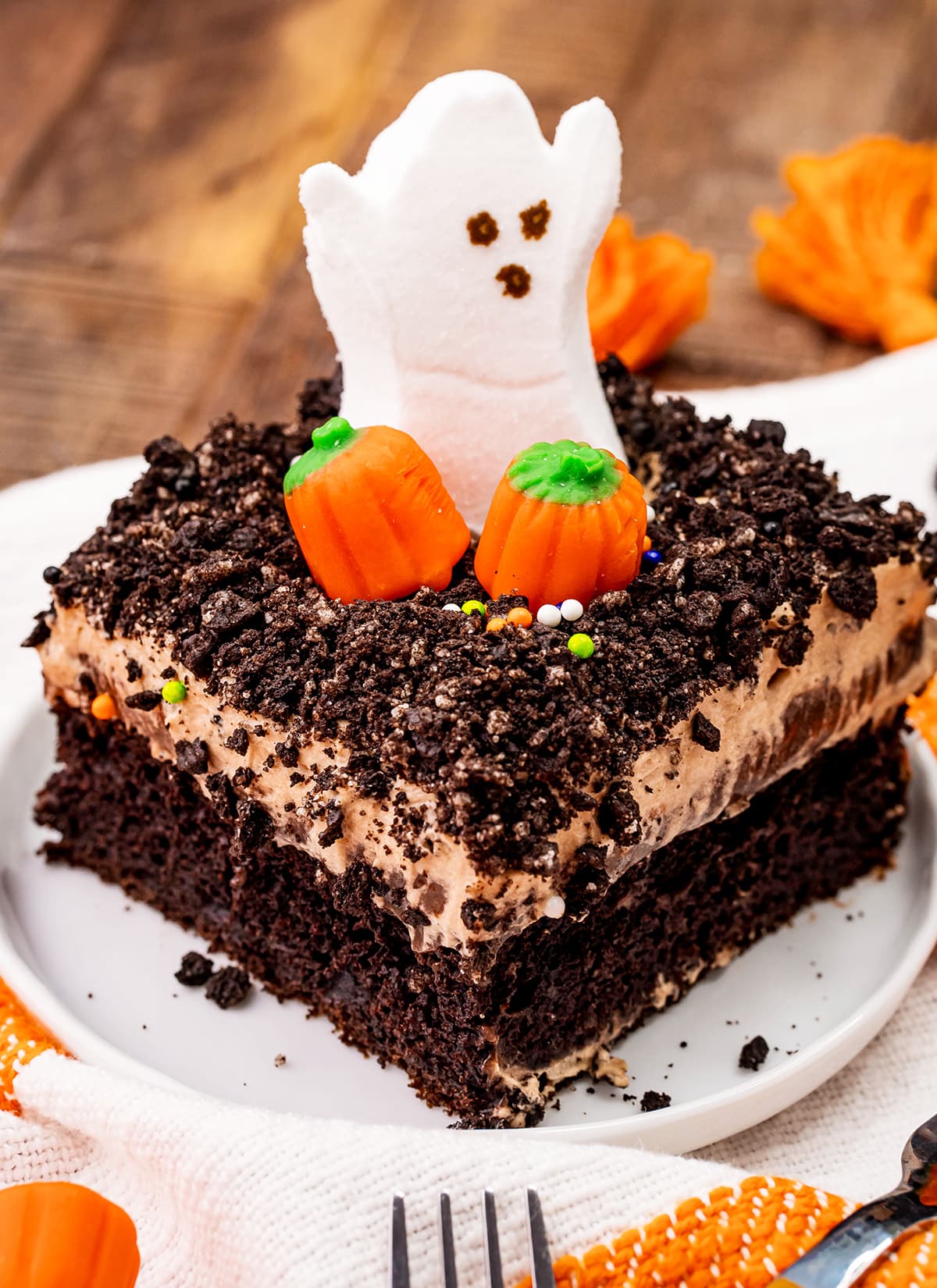 A slice of a chocolate poke cake topped with two candy pumpkins and a Ghost Marshmallow peep.