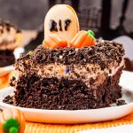 A slice of a Halloween Dirt Cake on a plate topped with a "gravestone" cookie and candy pumpkins, and Oreo crumbs.