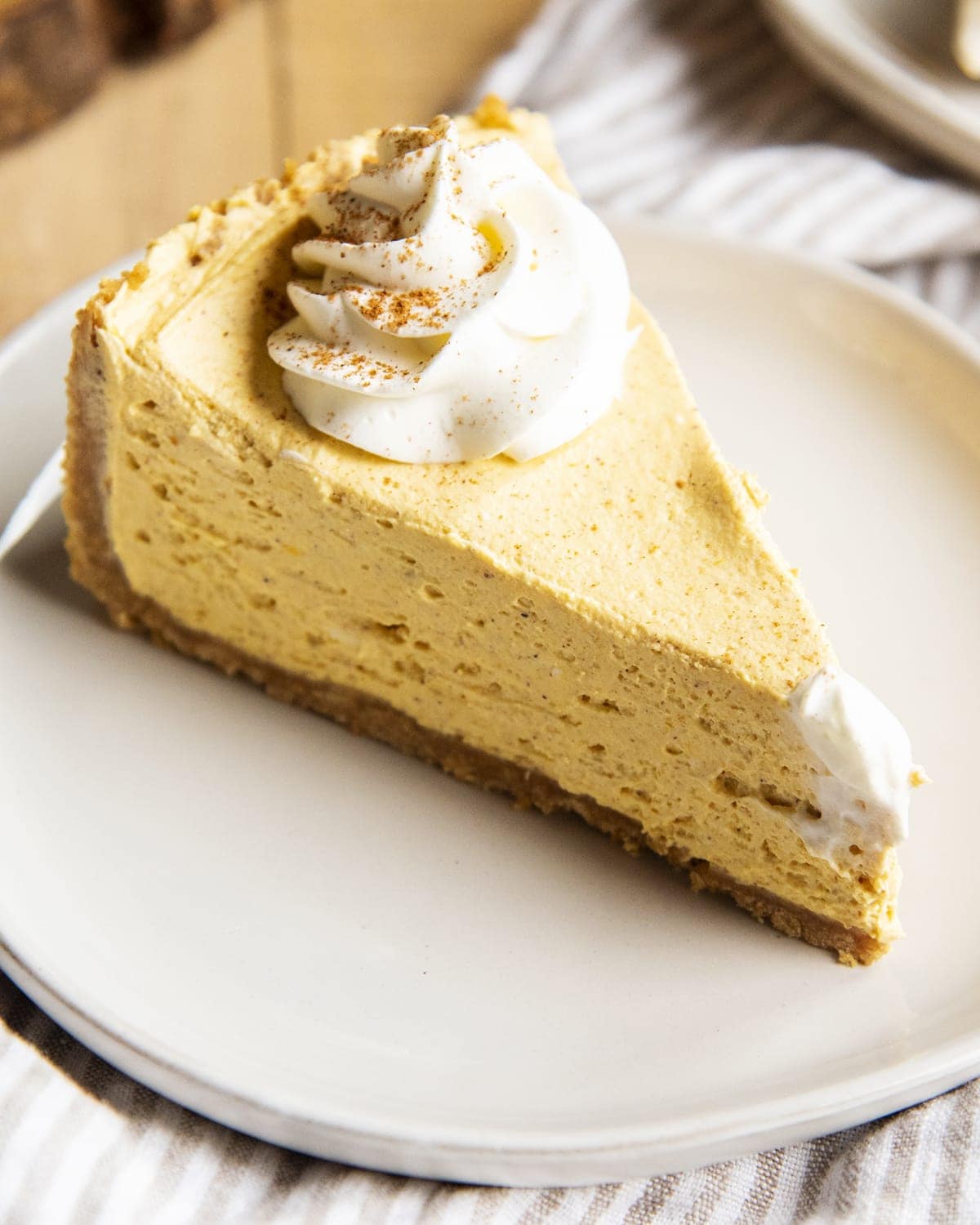 A slice of no bake pumpkin cheesecake, topped with a dollop of whipped cream and a sprinkle of cinnamon.