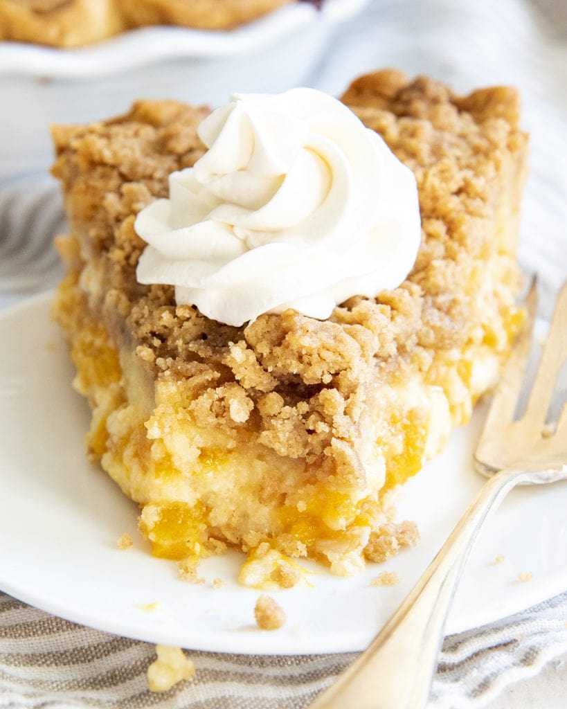 A piece of peaches and cream pie with a streusel topping, and whipped cream on top. A bite is taken out of the piece.