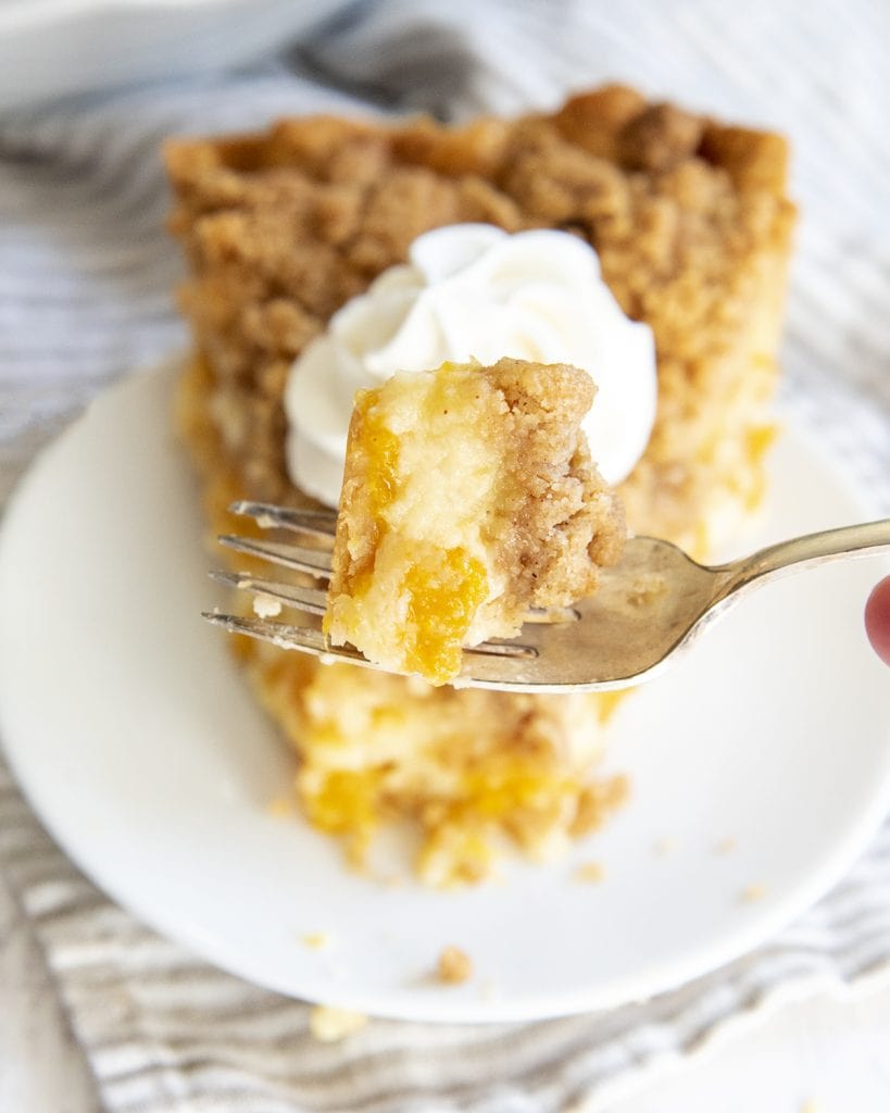 A bite of custard peach pie on a fork above a piece of the pie.