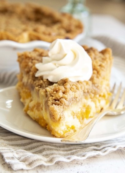 A slice of sour cream peach pie topped with a swirl of whipped cream.