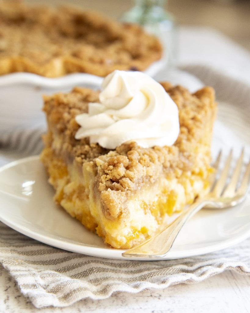 A slice of sour cream peach pie topped with a swirl of whipped cream.