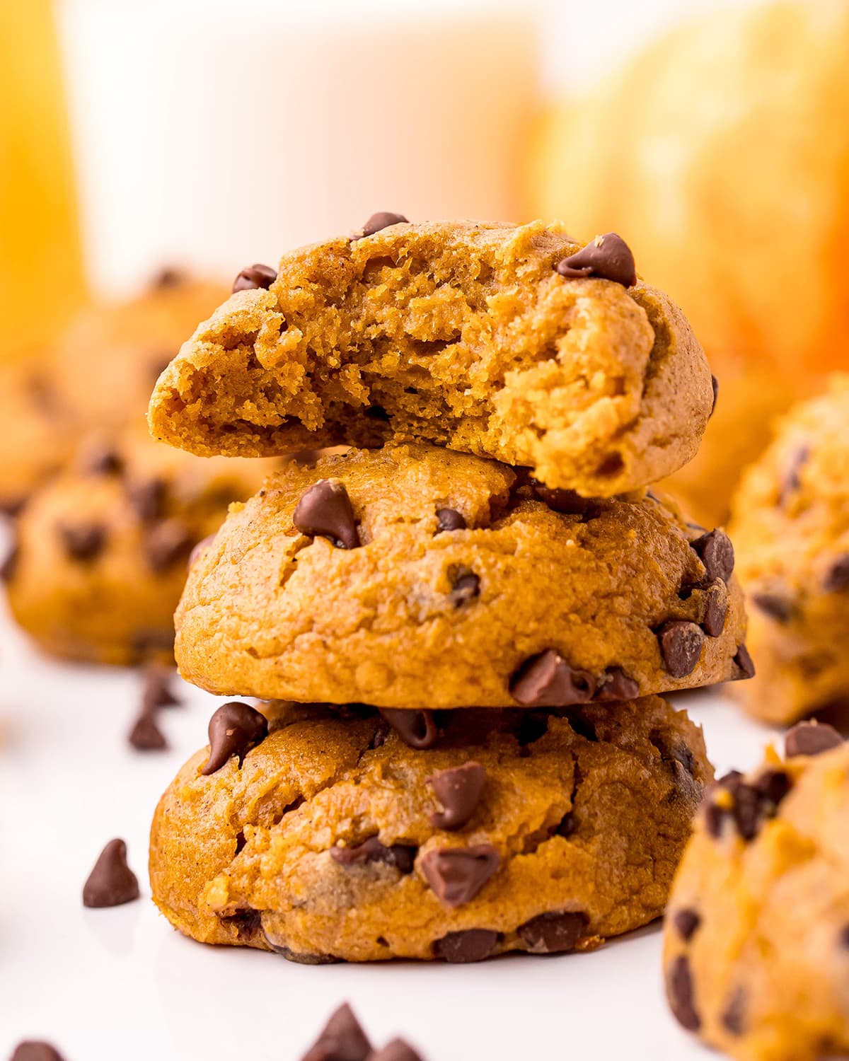 A stack of pumpkin chocolate chip cookies, with the top cookie has a bite out of it.