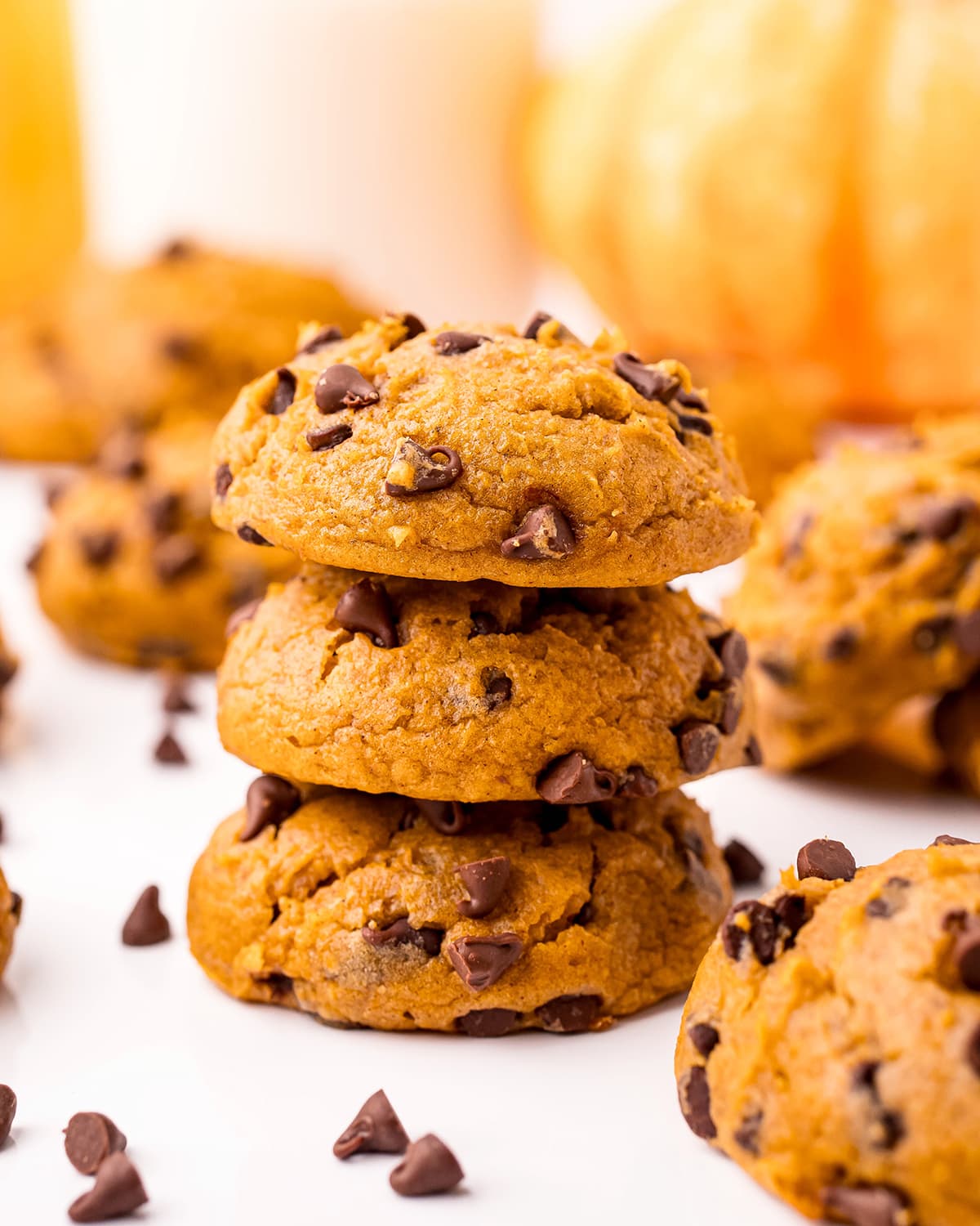 A stack of three pumpkin chocolate chip cookies with other cookies around it.