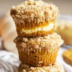 A stack of 3 pumpkin cream cheese muffins with a streusel crumb on top.