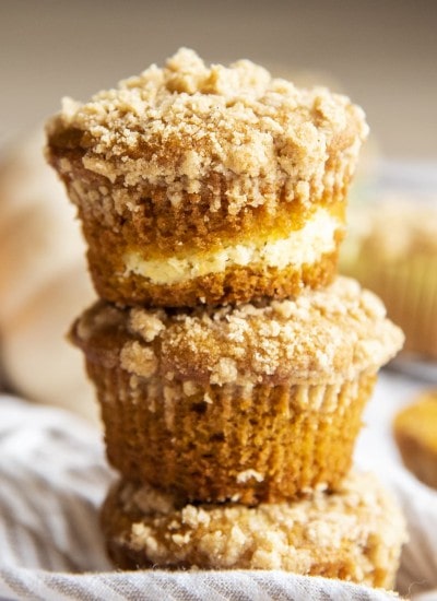 A stack of 3 pumpkin cream cheese muffins with a streusel crumb on top.