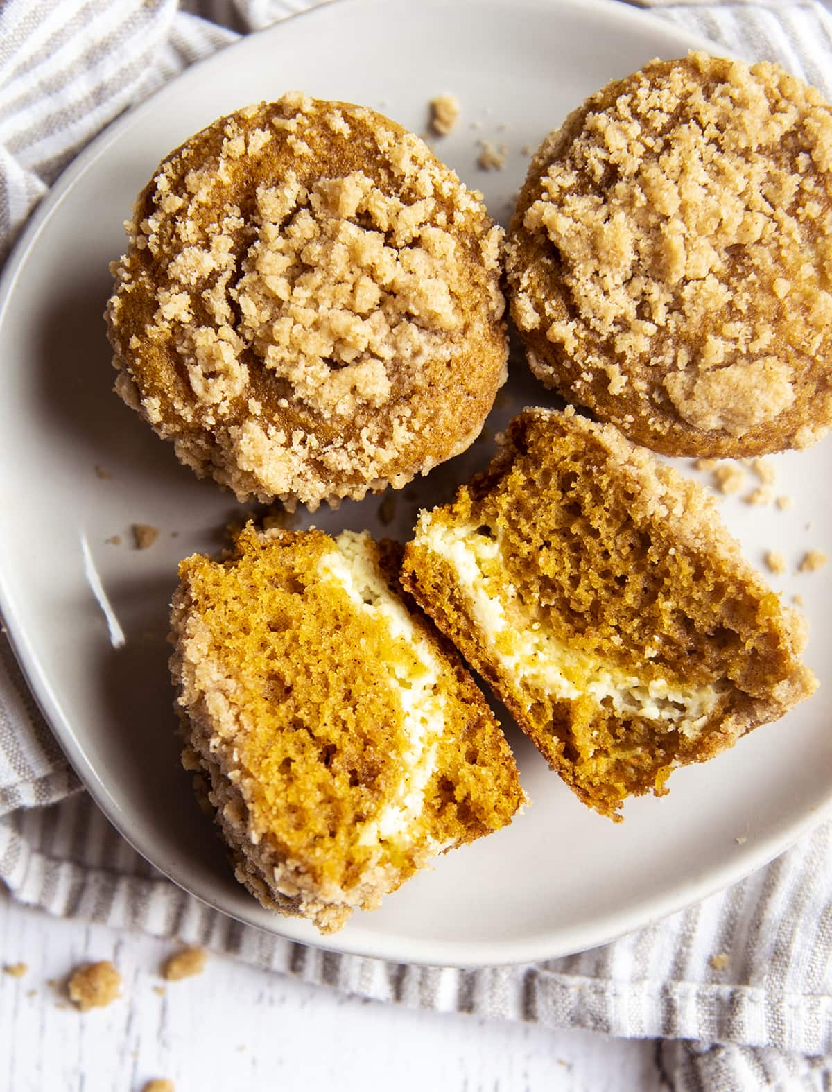 A plate of pumpkin cream cheese muffins, and one is cut in half showing the middle of the muffin and the cream cheese swirl.