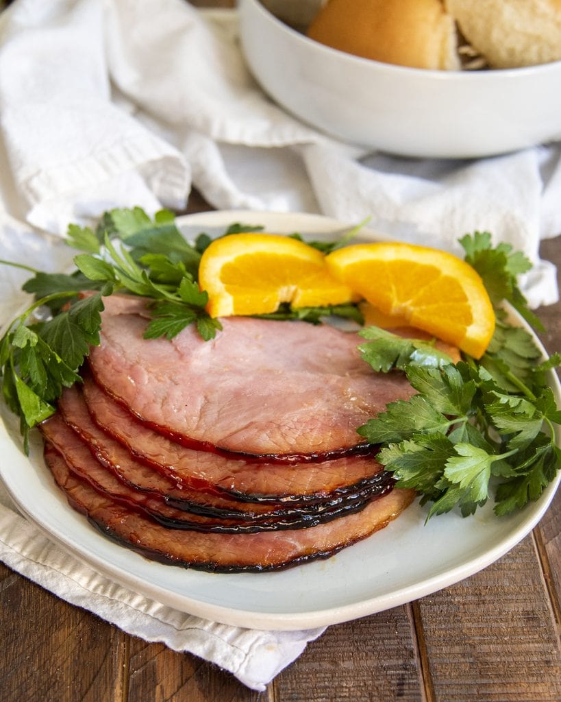 Slices of ham on a plate with fresh parsley and orange slices laying next to them.