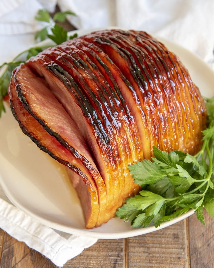 A spiral half ham on a plate covered in a shiny glaze, and laid next to parsley.