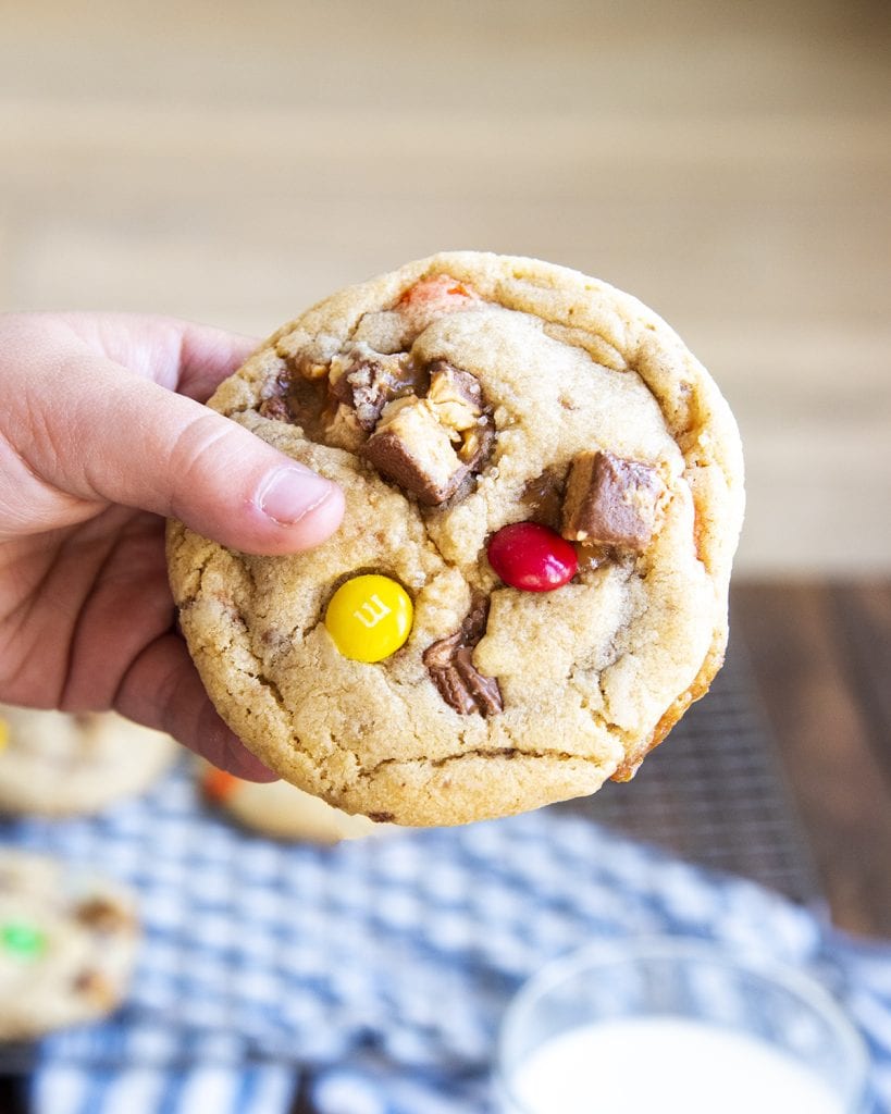 A child's hand holding a cookie that is full of chopped up chocolate bar pieces.