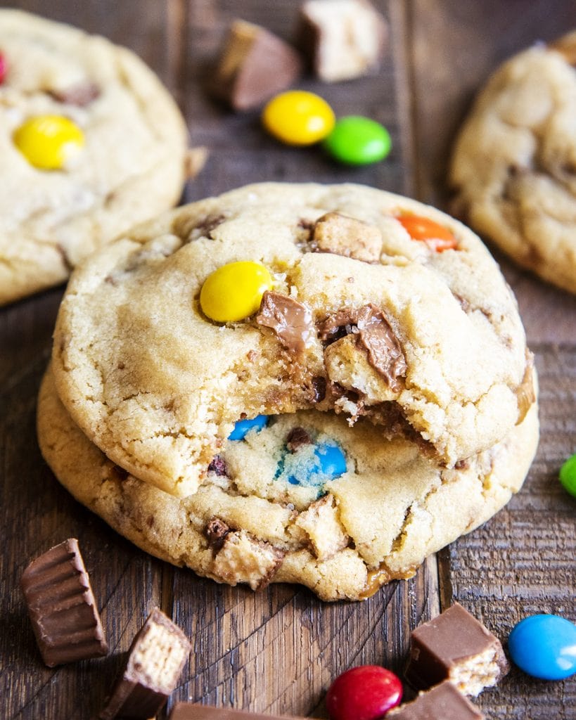 Two candy bar cookies stacked, the top cookie has a bite out of it, showing the gooey caramel of a melted candy bar piece.
