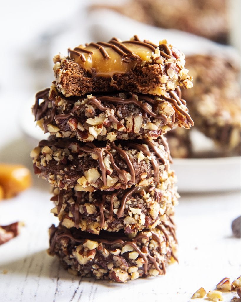 A stack of chocolate turtle cookies with caramel on the top of them, and drizzled with melted chocolate.