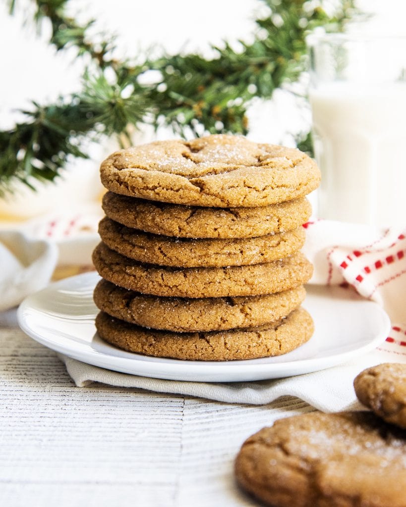 A stack of ginger molasses cookies on a white plate, with a glass of milk behind them.