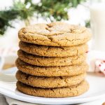 A stack of ginger molasses cookies on a white plate, with a glass of milk behind them.