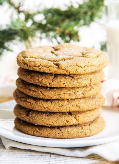 A stack of ginger molasses cookies on a white plate, with a glass of milk behind them.