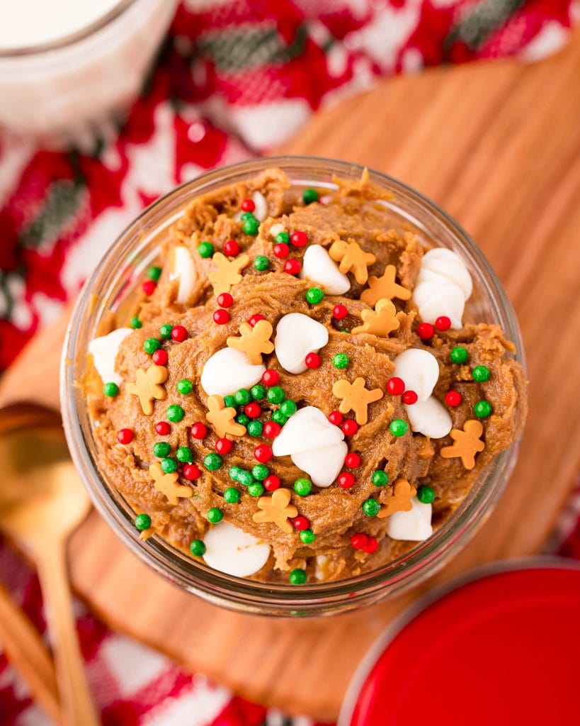 An overhead shot of gingerbread cookie dough in a jar, full of white chocolate chips and red and green sprinkles.