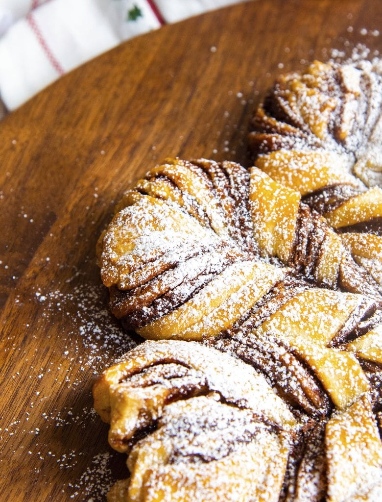 A close up of a twist of homemade Nutella Star bread, showing the twists of Nutella in the dough, all dusted with powdered sugar.