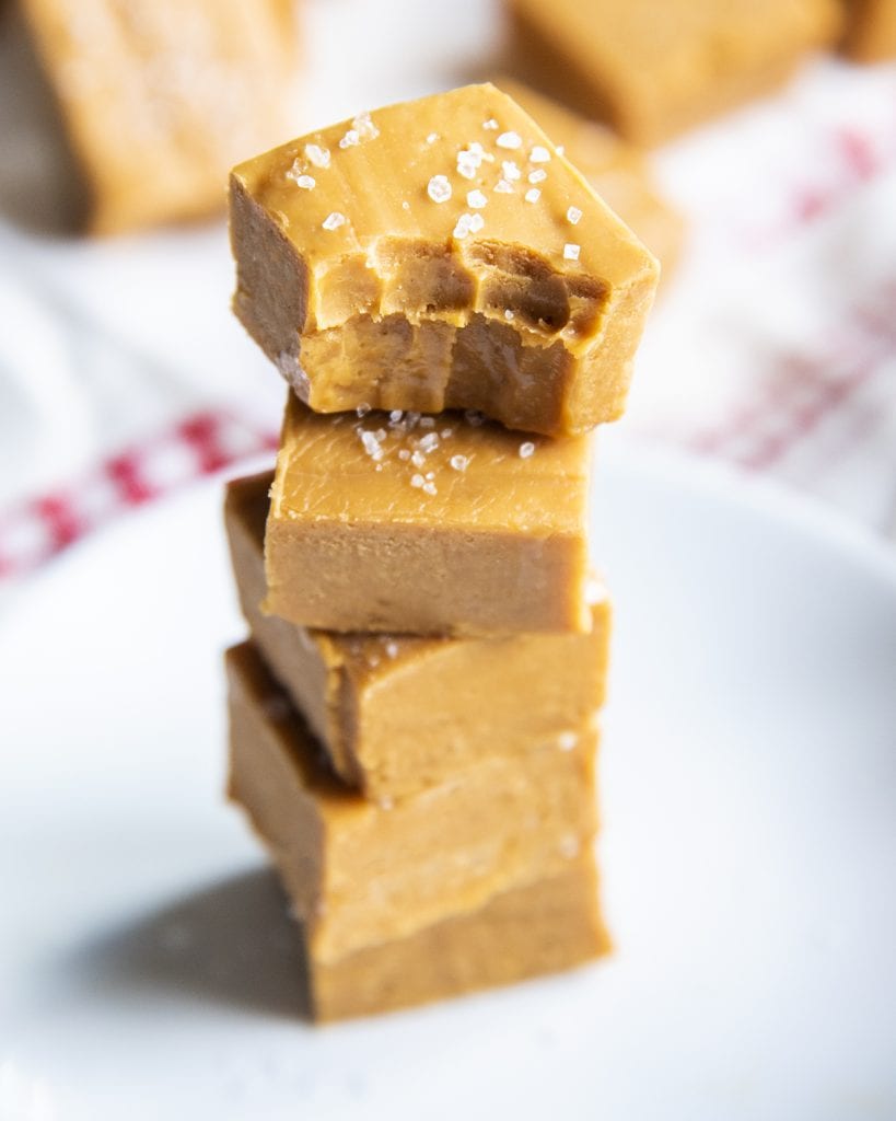 A stack of caramel fudge topped with sea salt. The top piece has a bite out of it.
