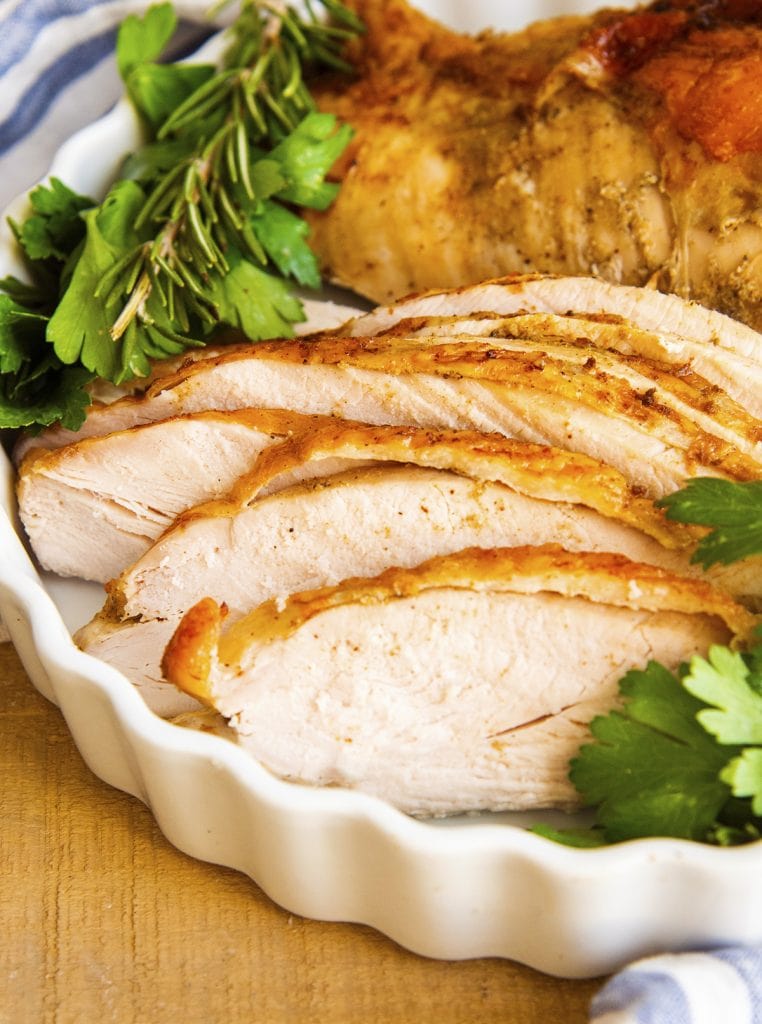 Slices of turkey breast topped with their skin laid out in a baking pan.