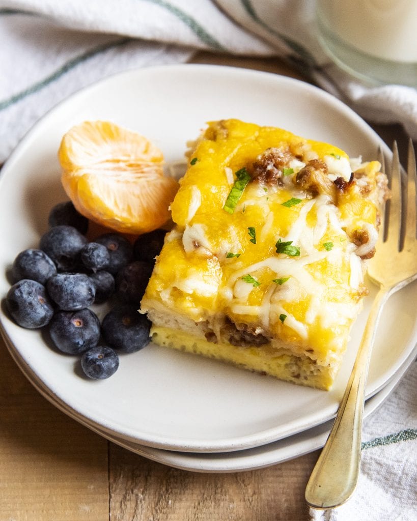 A piece of a biscuit sausage breakfast casserole on a plate with blueberries and half an orange.