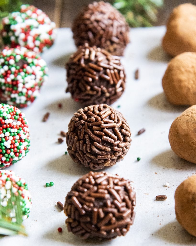Rows of chocolate truffles. The first row is covered in Christmas sprinkles, the second in chocolate sprinkles, the third in cocoa powder.