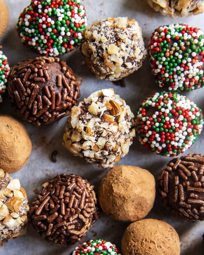 Chocolate truffles covered in sprinkles and nuts all spread on a parchment paper.