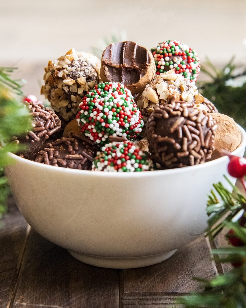 Chocolate truffles in a white bowl, the top truffle has a bite out of it showing the inside of the truffle.