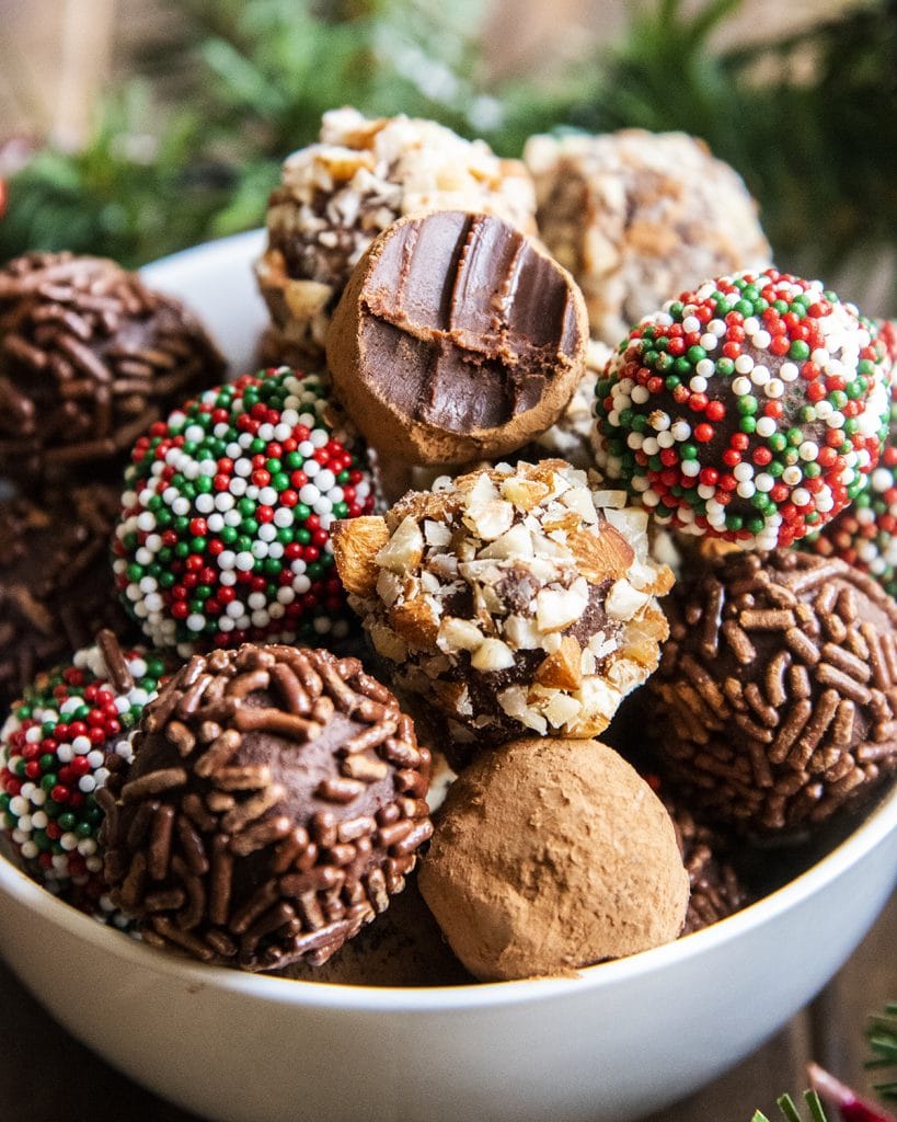 Chocolate truffles in a white bowl, the top truffle has a bite out of it showing the inside of the truffle.