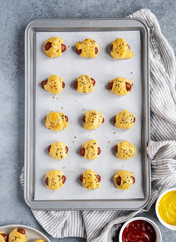 A cookie sheet covered in rows of pigs in a blanket wrapped in crescent roll and topped with everything bagel seasoning.