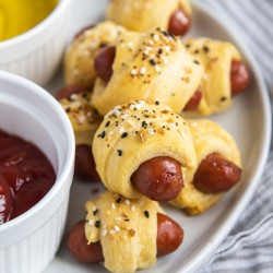 Pigs in a blanket topped with everything bagel seasoning on a plate.