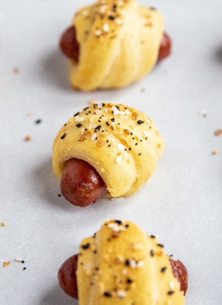 A close up of a little smokie hot dog wrapped in crescent roll and baked and topped with everything but the bagel seasoning.