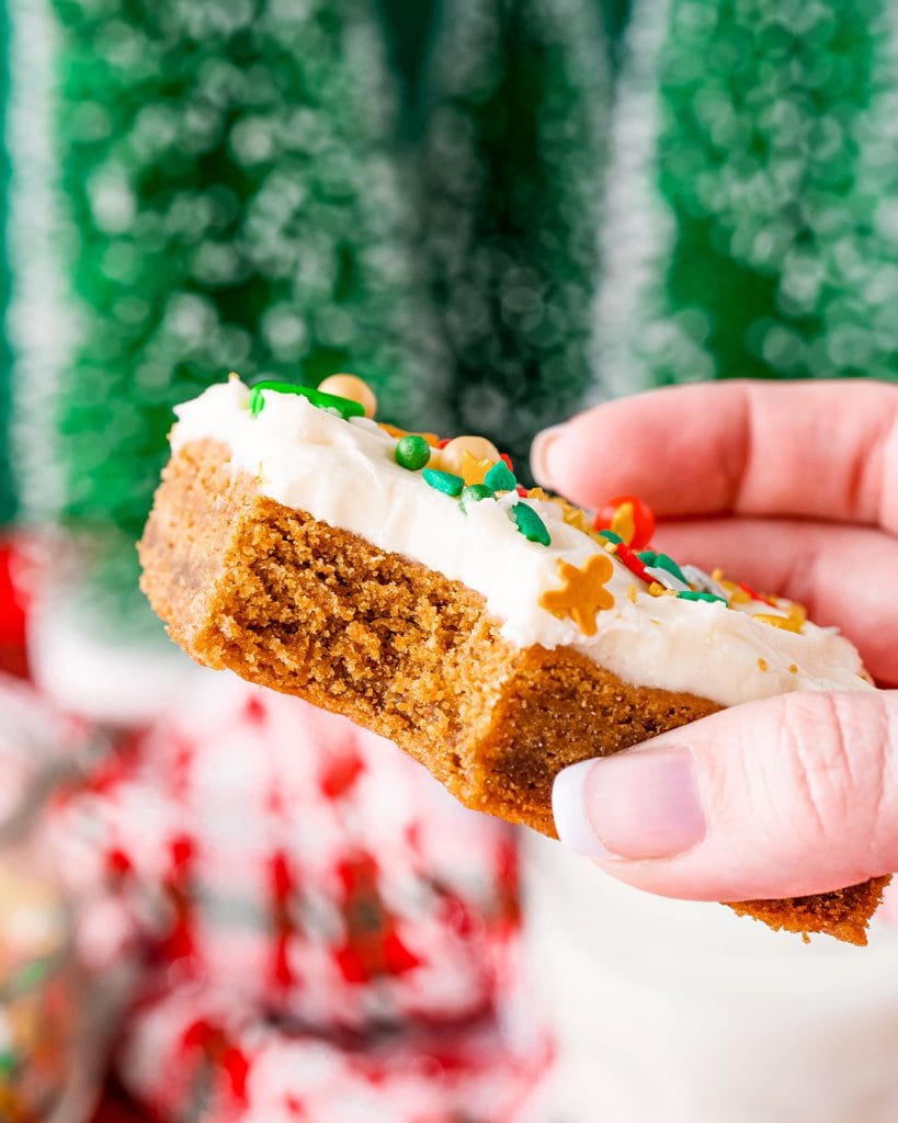 A hand holding a gingerbread cookie bar with a bite out of it.