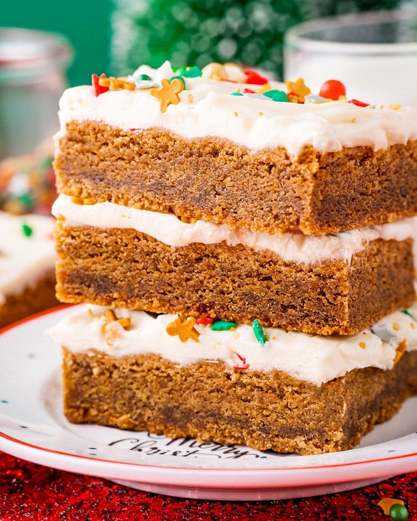 Three gingerbread bars topped with cream cheese frosting and sprinkles and stacked on a plate.