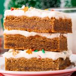 A stack of three gingerbread cookie bars topped with a white cream cheese frosting, and holiday sprinkles popping through.