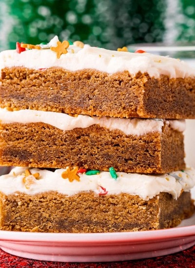 A stack of three gingerbread cookie bars topped with a white cream cheese frosting, and holiday sprinkles popping through.