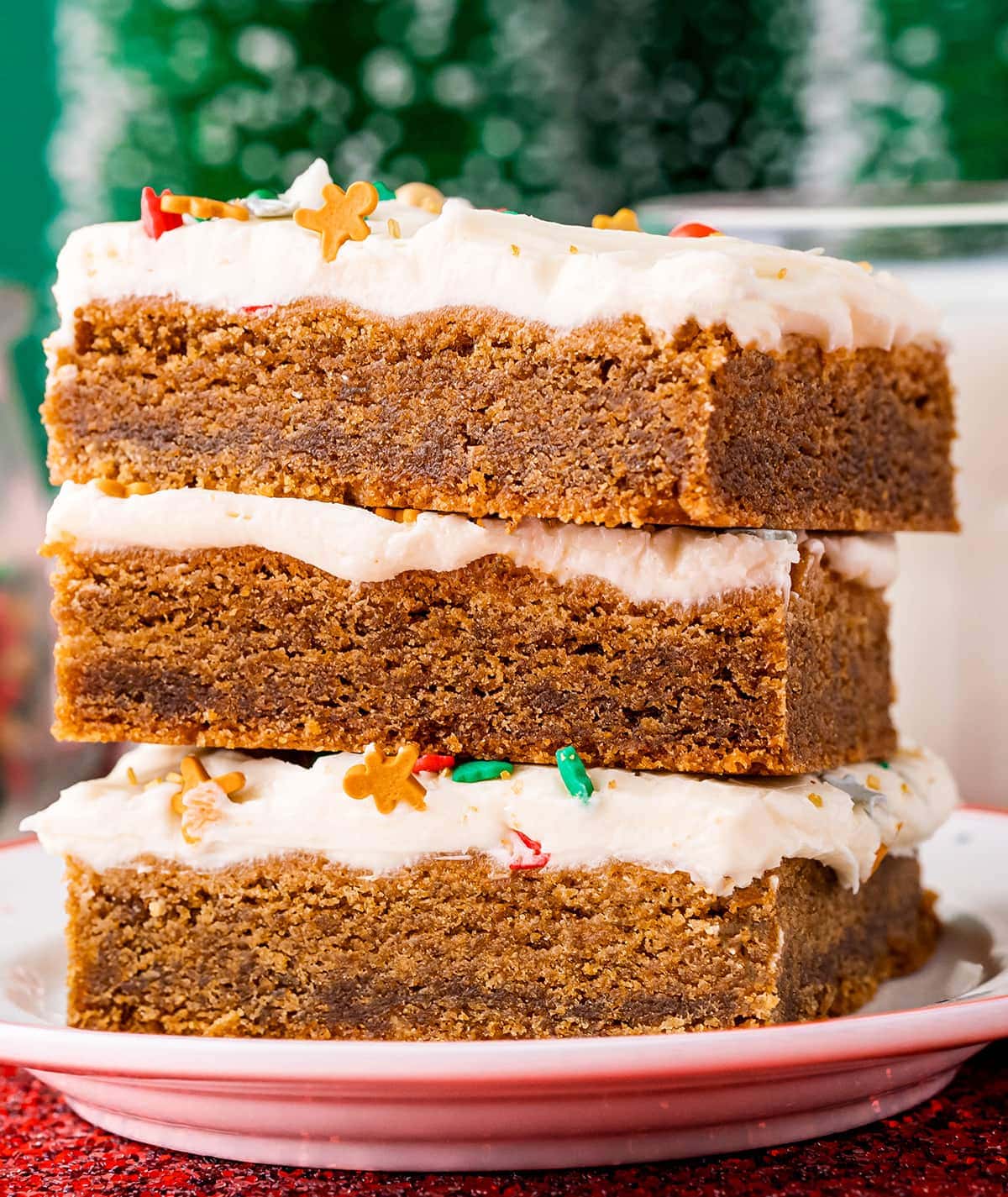 A stack of three gingerbread cookie bars topped with a white cream cheese frosting, and holiday sprinkles popping through.