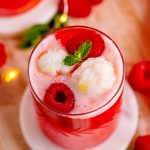 A cup of New Year's Eve Sherbet punch topped with sherbet, fresh raspberries, and mint leaves.