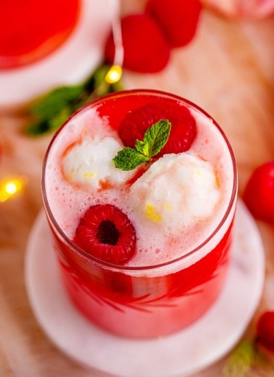 A cup of New Year's Eve Sherbet punch topped with sherbet, fresh raspberries, and mint leaves.